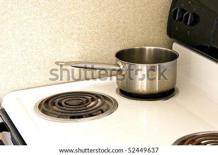 a stained stainless steel pan is sitting on top of an old dirty electric stove with linoleum from the 1950\'s on the wall, morning light