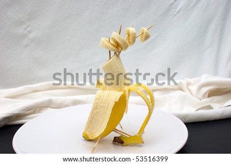 studio set up of sliced banana being propped up with toothpicks, with a light cloth background resting on plate