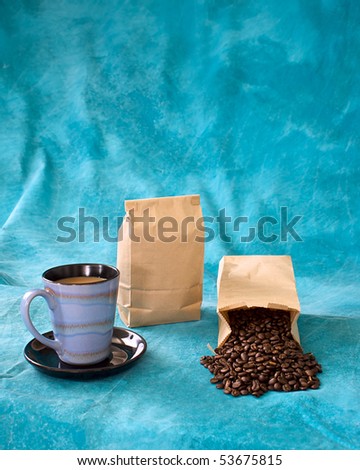 a fresh cup of coffee  in a blue cup with saucer, with coffee beans coming out of bag and a blank bag standing, add your logo. Also copy space above on mottled blue background