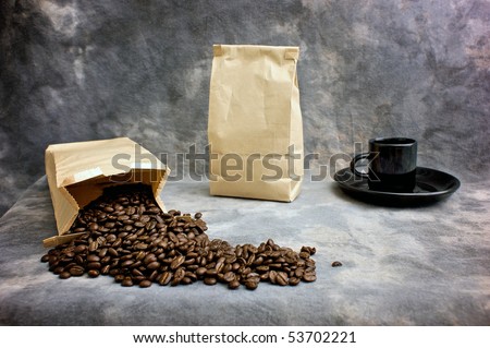 Fine art image of coffee showing a bag of whole beans, a closed bag of coffee and a black espresso cup on a saucer against a mottled studio background. Logo or text can be placed on blank bag.