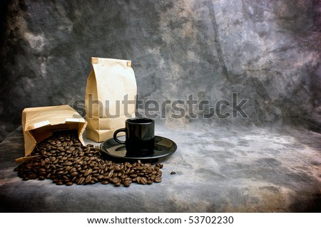 Fine art image of coffee showing a bag of whole beans, a closed bag of coffee and a black espresso cup on a saucer against a mottled studio background.  Logo or text can be placed on blank bag.