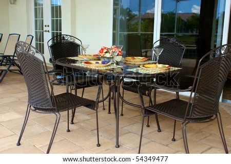 a table is set for dinner on an outside patio or lanai with sliding glass doors in the background