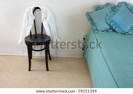 view of a simple room with small bed and old chair with white shirt on chair