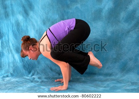 left side view of woman in Crow yoga pose against a blue background accented with blue and red lights.
