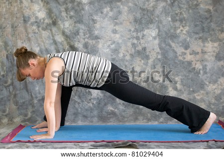 Young woman on yoga mat  doing Yoga posture lunge pose against a grey background in profile, facing left lit by diffused sunlight.