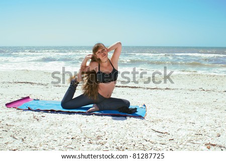an athletic brown haired woman is doing yoga exercise on beach in Kapotasana or Pigeon Pose on an empty beach at the gulf of mexico in bonita springs florida with long hair blowing in wind