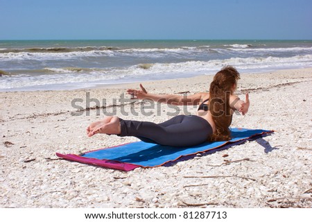 an athletic brown haired woman is doing yoga exercise Shalabhasana or locust  pose on an empty beach at the gulf of mexico in bonita springs florida