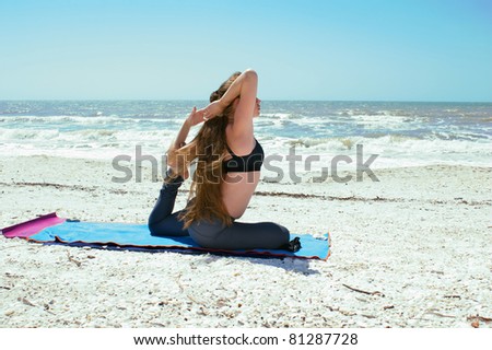 an athletic brown haired woman is doing yoga exercise on beach in Kapotasana or Pigeon Pose with foot in elbow  on an empty beach at the gulf of mexico in bonita springs florida with long hair bl