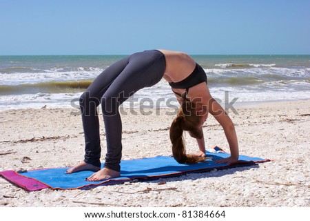 an athletic brown haired woman is doing yoga exercise full wheel pose or Urdhva Dhanurasana also known as upward bow posture on an empty beach at the gulf of mexico in bonita springs florida