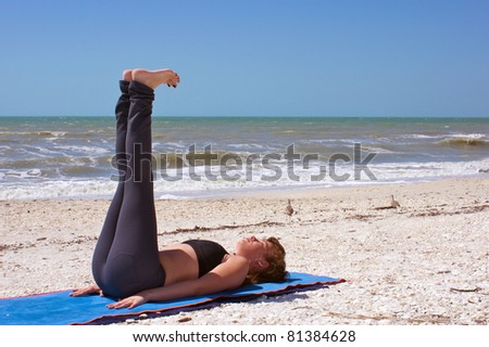 an athletic brown haired woman is doing yoga exercise reclined staff pose on an empty beach at the gulf of mexico in bonita springs florida
