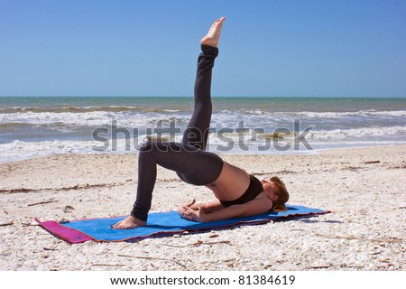 an athletic brown haired woman is doing yoga exercise one leg bridge pose on an empty beach at the gulf of mexico in bonita springs florida