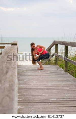 an athletic brown haired woman is doing yoga exercise rotated awkward chair pose on an empty beach at the gulf of mexico in naples florida at sunset