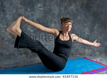 A brown haired caucasian woman is smiling doing yoga exercise, Navasana Pose or Rotated Boat posture  on yoga mat in studio with mottled background.