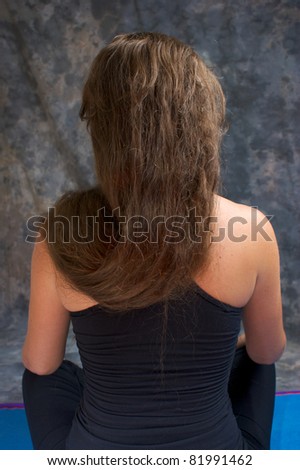 A white woman with long brown hair seen from behind sitting with hair draped over shoulder.