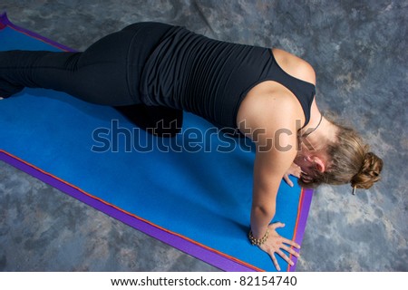 Looking down on an athletic brown haired woman is doing yoga exercise low lunge pose on yoga mat in studio with mottled background.