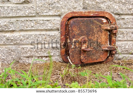 An old rusted iron door sits close to the ground on the outside wall of a stone brick chimney.