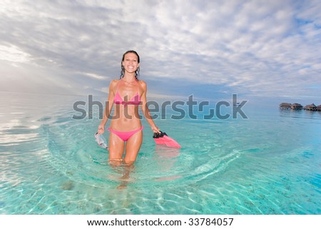 Woman with snorkel gear near tropical resort beach in pink bikini smiling