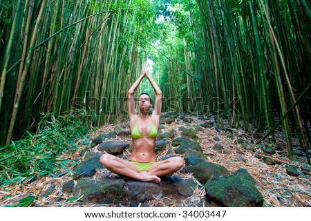 Woman in green bikini doing yoga meditation relaxing on bamboo path in hana maui rain forest