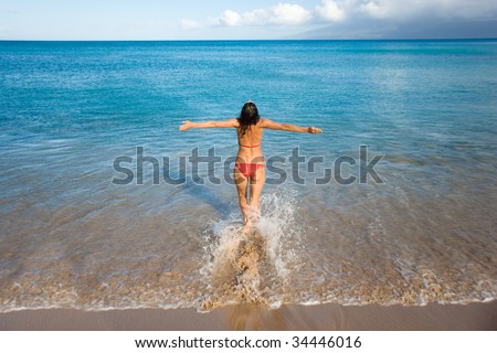 woman on beach in red bikini standing free in turquoise waters happy and free in maui, hawaii