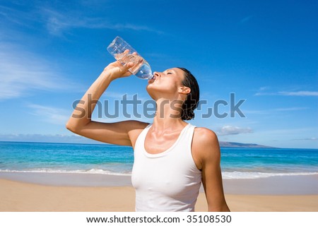 woman in white yoga outfit drinking fresh water form sport bottle after exercise on tropical beach