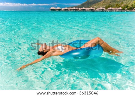 beautiful woman floating in turquoise waters near tropical resort
