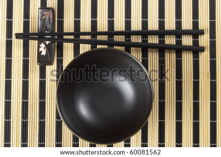 Wooden chopsticks and little ceramic bowl on the bamboo mat background