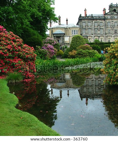 A small lake in a beautiful English garden, with a manor house in the background
