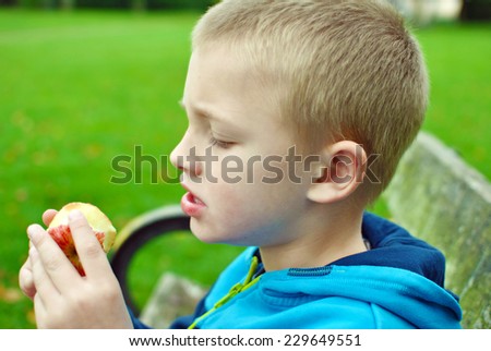 seven year old boy eating apple in the park