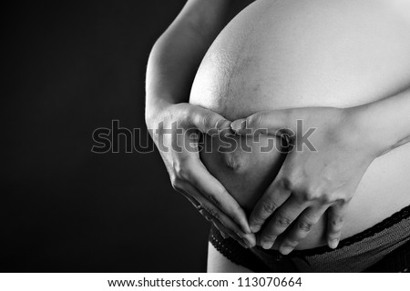 Black-white image of pregnant woman touching her belly with hands on black background
