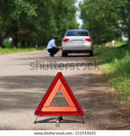 The image of emergency stop sign under the foreground and man near car under background. Focus is under the sign.