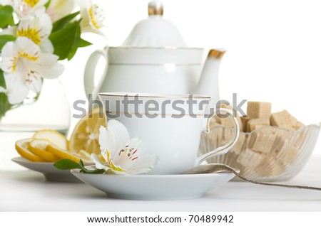 Cup of tea and teapot on table with flowers isolated over white