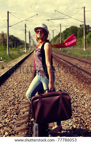 cross process technique reproduction showing beautiful young girl walking on railroad tracks with suitcase and  hat in casual