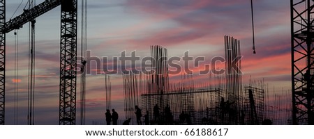 silhouettes of construction workers, construction equipment and elements of a building under construction at Sunset