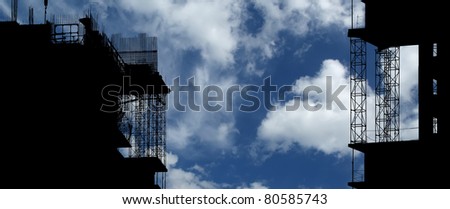 Silhouette of construction, construction equipment and elements of the building under construction on the sky background