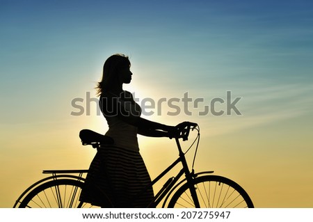 Woman with bike. Silhouette against the sky.