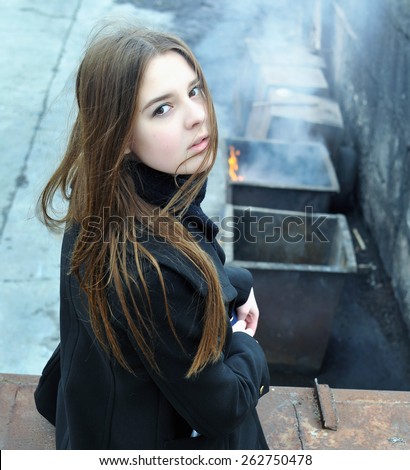 Girl sitting on the roof of the garage on the background of a burning dumpster