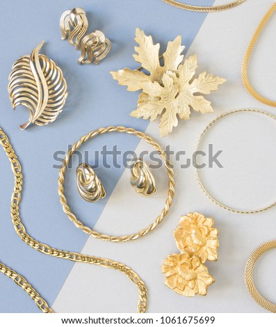 Woman\'s Jewelry. Vintage jewelry background. Beautiful gold tone brooches, braceletes, necklaces and earrings on blue background. Flat lay, top view