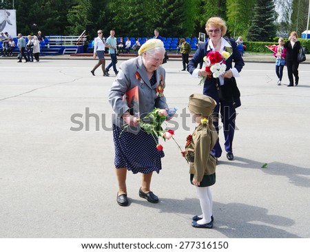 OMSK, RUSSIA -  MAY, 9, 2015: Celebration of 70th anniversary of Victory.\
Woman veteran receives congratulations from little girl in uniform.