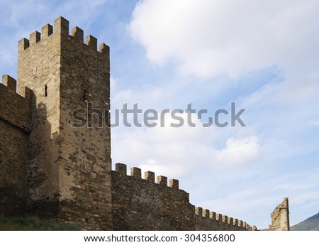 Crimea , Sudak Genoese fortress, ancient fortification of middle ages, defensive jagged stone wall and tower closeup against blue cloudy sky