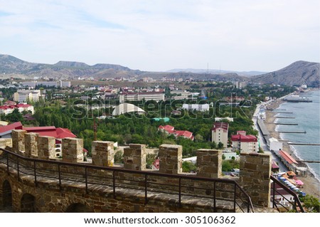 SUDAK, RUSSIA  - SEPTEMBER 27, 2014: Top view of township, shoreline and mountain scenery surroundings,   merlons of ancient wall of Genoese fortress on foreground