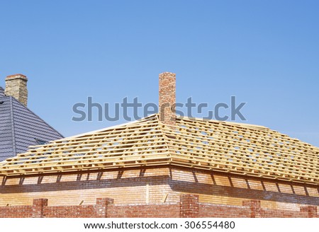Wooden planks frame of new roof and brick chimney of cottage under construction