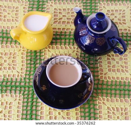 crockery on knitted cloth.cup of beverage, jug with milk and teapot