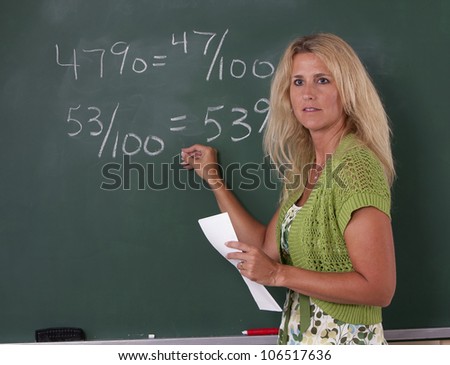 Math teacher in classroom at chalkboard teaching fractions.