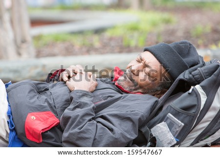 Old african american homeless man sleeping outside during the day.