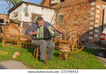 Ukrainian country-man playing button accordion (garmon) while having a short rest at summer evening