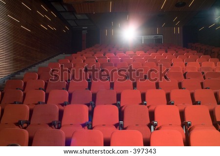 Back-lighted theater interior showing several rows of empty red seats