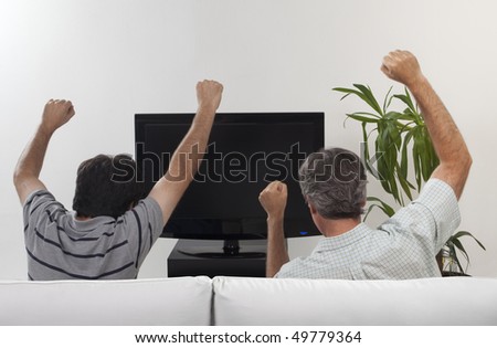 Two friends celebrating some event watching a flat tv set sitting on a sofa