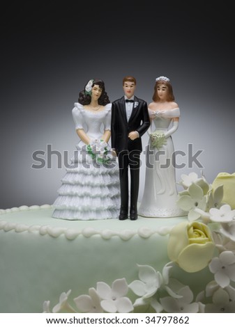 stock photo Groom and two bride figurines on top of wedding cake