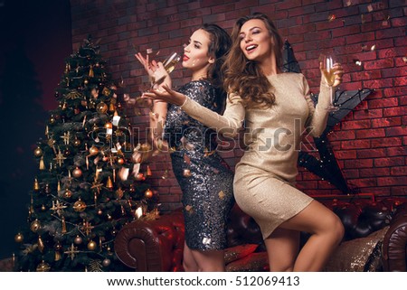 Portrait of two smiling girl with tinsel confetti in hands and wineglasses with champagne. New year\'s feeling. Merry christmas