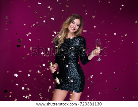 Portrait of attractive smiling girl with tinsel confetti in hands bottle of champange and wineglasses with champagne. New year\'s feeling. Merry christmas. Happy woman celebrate holiday